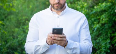 İş analistinin açık hava telefonuyla internet üzerinden çalışmasının kırpılmış görüntüsü.