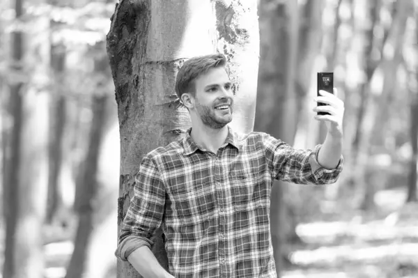 smiling man blogger take selfie on smartphone. photo of man blogger take selfie in the forest. man blogger take selfie outdoor. man blogger take selfie on phone.