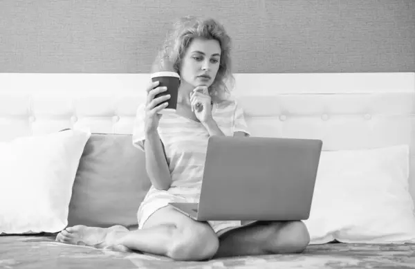 pensive woman freelancer with coffee work at home on laptop. freelancer woman work at home. home work for freelancer. woman in bed with laptop.