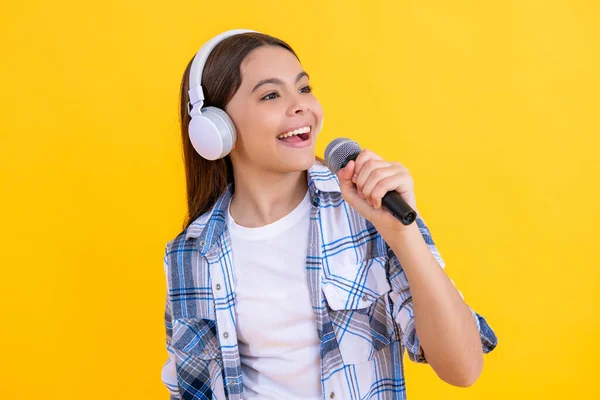 glad singer girl singing music on background. singer girl with microphone in music studio. talented music singer girl in headphones. young girl singing into music microphone isolated on yellow.