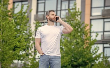 Sokakta telefonla konuşan sıradan bir adam. Dışarıdaki adam aradı. Adamın telefonla arayıp konuştuğu bir fotoğraf. Adamın dışarıda telefonu var..