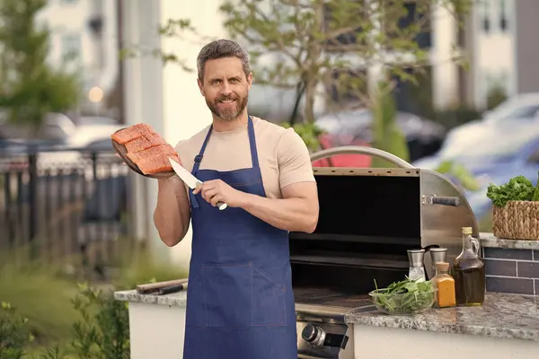 happy man with grill salmon. man cook salmon on grill. chef man cooking salmon on grill outdoor. grill salmon fish at man wear apron.