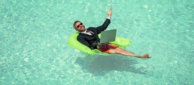 Neşeli iş adamı internette ticaret yapıyor. Yüzme havuzunda ticaret yapan bir iş adamı. İşadamı bilgisayarla online ticaret yapıyor. İş adamının internetten takım elbise alışverişi fotoğrafı..