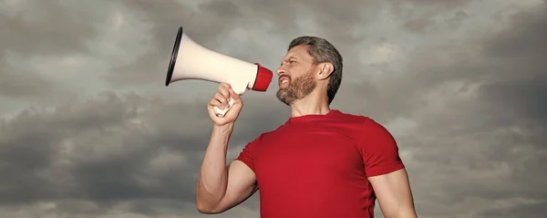 man in red shirt speaking in loudspeaker on sky background.