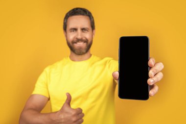 Akıllı telefon uygulaması gösteren adam sarı, seçici odak noktasında izole edilmiş. Adam arka planda akıllı telefon uygulaması gösteriyor. Stüdyoda akıllı telefon uygulaması gösteriyor. Akıllı telefon uygulaması gösteren bir adamın fotoğrafı.