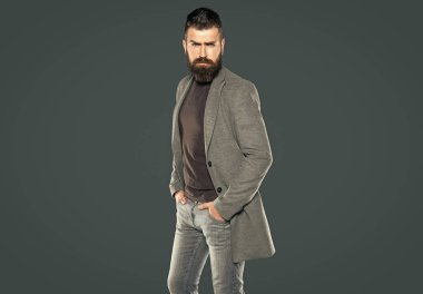 Sakallı yetişkin adam gri arka planda günlük giyiniyor..