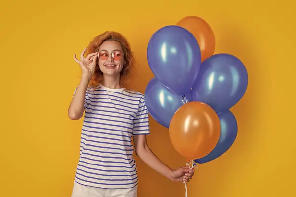 happy woman with birthday balloon in sunglasses. happy birthday woman hold party balloons in studio. woman with balloon for birthday party isolated on yellow background.