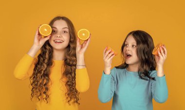 Genç kızlar gülümseyerek sarı arka planda portakal meyvesi tutarlar. çekici turuncu kızlar,