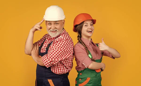 stock image happy girl and grandfather builder in helmet on yellow background. thumb up. builder concept. fathers day