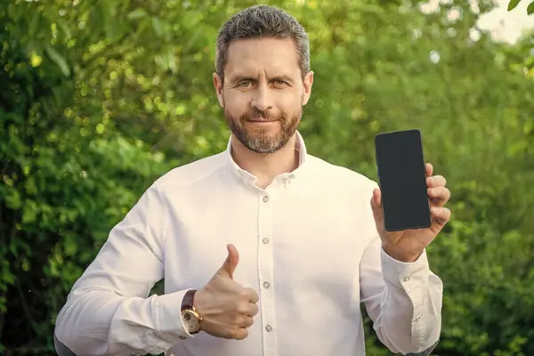 businessman showing app outdoor, thumb up. businessman showing app on phone. businessman showing app with copy space. businessman showing app.