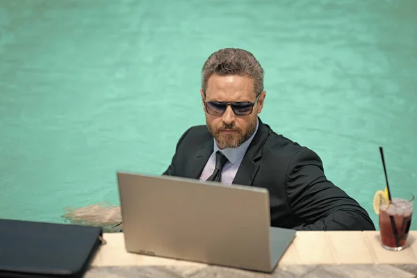 business man working remote online. business man working remote in swimming pool. business man working remote with laptop. business man working remote in summer pool