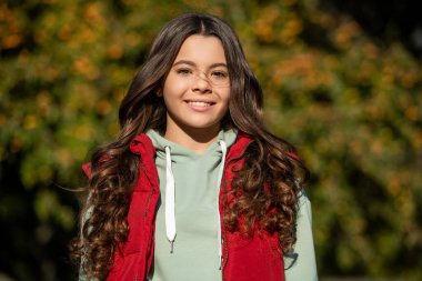 Kıvırcık kız dışarıda portrede gülümsüyor. Güneşli bir günde genç kız portresi. Kıvırcık bir genç kızın portresi. Açık havada genç kız portresi.