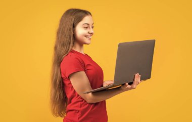 Sarı arka planda dizüstü bilgisayarı olan neşeli çocuk..