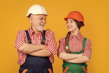 Mutlu çocuk ve büyükbaba sarı arka planda kalın şapkalı inşaatçı.