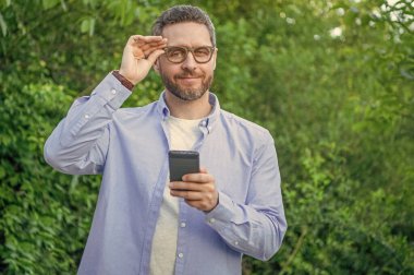 Gülümseyen adam telefonda mesaj atıyor, kopyala uzayı. Adam dışarıda telefonla mesajlaşıyor. Telefonla mesajlaşan ya da e-postaları kontrol eden bir adam. Telefonda mesajlaşan adamın fotoğrafı..