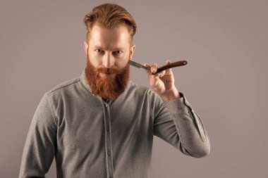 Gri arka planda berber bıçağıyla tıraş olan bir adam, kopyalama alanı. Berber adam bıçakla tıraş oluyor. Berber stüdyosundaki adam. Adam tıraş olmak için berber bıçağını tutuyor..