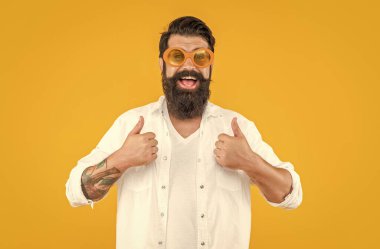Havalı hippi stüdyoda baş parmağını gösteriyor. Arka plandaki havalı hippi adam. Havalı hippi adamın güneş gözlüğü taktığı fotoğraf. Havalı hippi adam sarıda izole edilmiş..