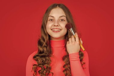 Kıvırcık saçlı mutlu çocuk makyaj fırçasıyla yüzüne pudra sür.