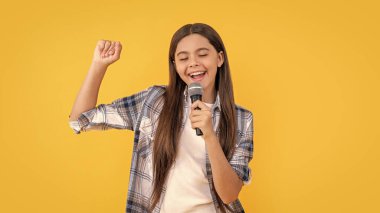 Stüdyoda neşeli genç kız karaoke şarkıcısı. Genç kız karaoke şarkıcısı. Genç kız karaoke şarkıcısının mikrofonlu fotoğrafı. Genç kız karaoke şarkıcısı sarıda izole edilmiş..