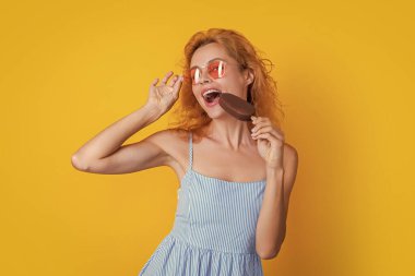 Kadın stüdyoda dondurma yiyor. Arkasında dondurma olan bir kadın. Yazın dondurmalı kadın. Dondurmalı kadın sarıda izole edilmiş.