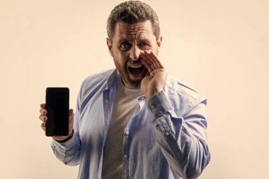 Çığlık atan adam telefon uygulaması gösteriyor. Telefon uygulaması gösteren adamın fotoğrafı. Stüdyonun arka planında izole edilmiş bir telefon uygulaması var. Stüdyoda telefon uygulaması gösteren adam.