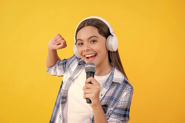 smiling music singer girl in headphones. young girl singing into music microphone isolated on yellow. teenage singer girl singing music on background. singer girl with microphone in music studio.