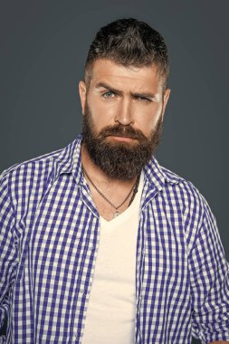 Sakallı adamın yüzü gri arka planda kareli gömlek giyer..