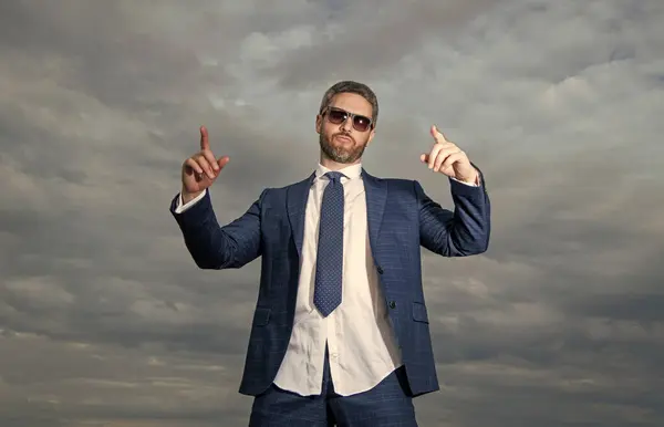 carefree business man point finger in suit. photo of carefree business man in suit. carefree business man in suit on sky background. carefree business man in suit outdoor.