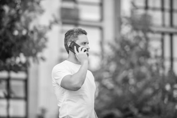 mature man having phone call in the street. man call on phone outside. photo of man call on phone and talk. man has phone call outdoor.