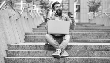 Dışarıda serbest iletişimi olan mutlu bir adam. Açık havada serbest iletişimde olan bir adam. Serbest çalışan bir adam telefonda konuşuyor. Dizüstü bilgisayarında serbest iletişimi olan bir adam..