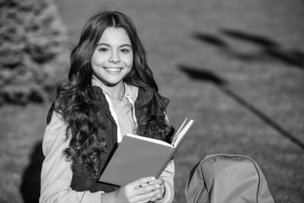 school teen girl smile and read outside. school teen girl read book. photo of school teen girl read in park. school teen girl read outdoor.
