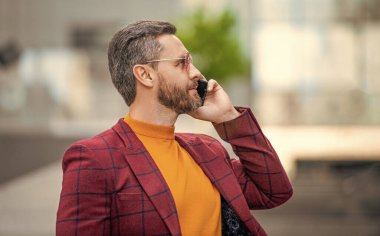 Adamın dışarıda cep telefonu görüşmesi var. Sokakta cep telefonu arayan bir adam var. Dışarıdaki cep telefonundan arayan bir adam. Adamın cep telefonuyla arayıp konuştuğu bir fotoğraf..