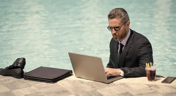 business man working remote in swimming pool, banner. business man working remote with laptop. photo of business man working remote in summer pool. business man working remote online.