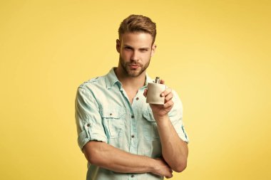 Stüdyonun arka planında kolonya tutan adam. Erkek parfümünün fotoğrafı. Adam kolonyayı tutuyor. Kolonyayı sarı renkte tutan adam..