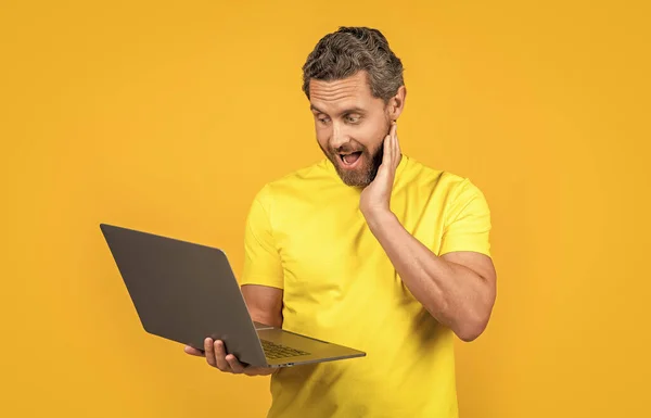 image of surprised man programmer with laptop. man programmer isolated on yellow. man programmer on background. man programmer in studio.