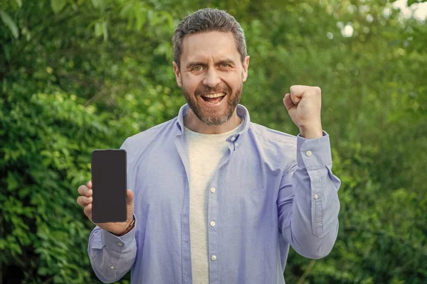 successful man presenting smartphone. man presenting smartphone outdoor. man presenting smartphone screen with copy space. photo of man presenting smartphone.