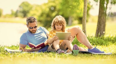 Oğlu ve babası yazın kaynaşıyorlar. Baba ve oğul eğitimi. Baba oğul eğitimini kitap tabletiyle şekillendirir. Baba ve oğul parkta. çocukluk okulu eğitimi. Eğitim doğayla birleşir.