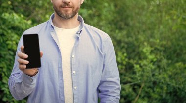 Akıllı telefon ekranını fotokopi aletiyle sunan adamın kırpılmış görüntüsü. Akıllı telefon sunan adamın fotoğrafı. Akıllı telefon sunan adam. Adam dışarıda akıllı telefon sunuyor..