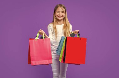 Arka planda alışveriş yapan gülümseyen genç kız. Alışveriş yapan genç bir kızın fotoğrafı. Alışverişi olan genç bir kız mor renkte izole edilmiş. Stüdyoda alışveriş yapan genç kız..