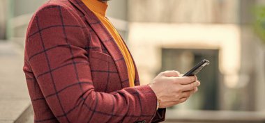 Sokakta akıllı telefondan mesajlaşan bir adamın görüntüsü. Dışarıda akıllı telefondan mesaj atan bir adam var. Akıllı telefondan ceketle mesaj atan adamın fotoğrafı. Adam açık havada akıllı telefondan mesaj atıyor..