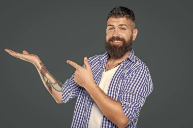 Sakallı adam, gri arkaplandaki kareli tişört parmağıyla fotokopi alanı takıyor..