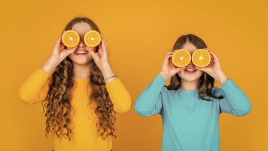 Komik genç kızlar sarı arka planda portakal meyvesi tutarlar..