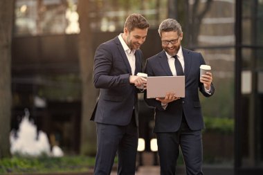 İşadamları online olarak bilgisayar ve reklamlarla ticaret yapıyor. İnternet üzerinden ticaret yapan iş adamlarının fotoğrafı. İki işadamı çevrimiçi ticaret yapıyor. İş adamları açık havada ticaret yapıyor.