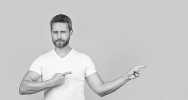 Gündelik tarzda parmakla işaret eden bir adam. Sarı arka planda izole edilmiş sıradan gömlekli sakallı bir adam. Stüdyoda sıradan bir adam. Beyaz gömlek giyen beyaz bir adamın fotoğrafı..