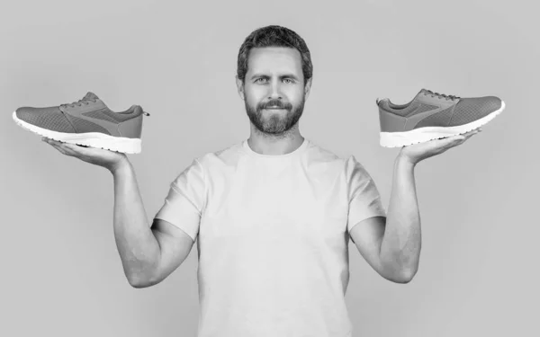 stock image positive fitness man with sneakers in studio. photo of fitness man with sneakers shoes. fitness man with sneakers isolated on yellow. fitness man with sneakers on background.