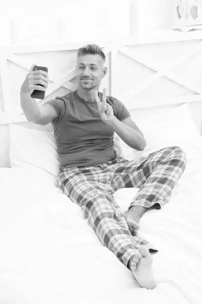 photo of blogging man with phone at home, peace. blogging man with phone in bedroom. blogging man with phone wear pajama. blogging man with phone in bed.