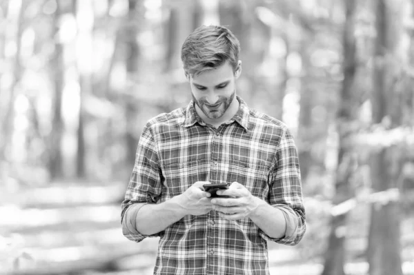 image of man messaging on phone in the forest. man messaging on phone outdoor. man messaging on phone outside. man messaging on phone wearing checkered shirt.