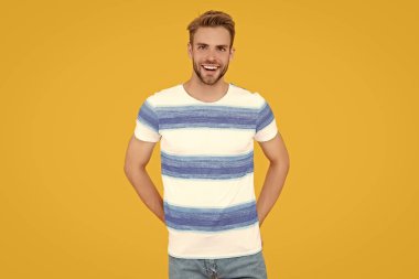 Yakışıklı bir adam neşeli görünen bir portre için poz verir. Sarı arka planda izole edilmiş sakallı genç adam. Şık bir stüdyo resmi. Bin yıllık insan portresi..