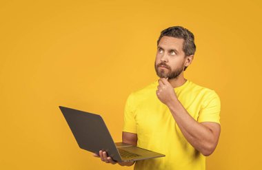 Stüdyoda serbest çalışan düşünceli bir adam. Dizüstü bilgisayarlı serbest çalışan bir adamın fotoğrafı. Serbest çalışan bir adam sarıda izole edilmiş. Arka planda serbest çalışan bir adam.