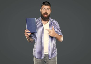 Şaşırmış sakallı adam gri arka plan hakkında kitap tavsiye ediyor. işaret parmağı.